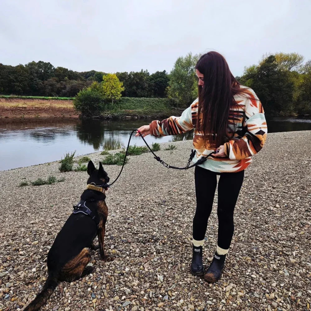 Woman holding handmade rPET dog lead attached to sitting dog by a riverbank