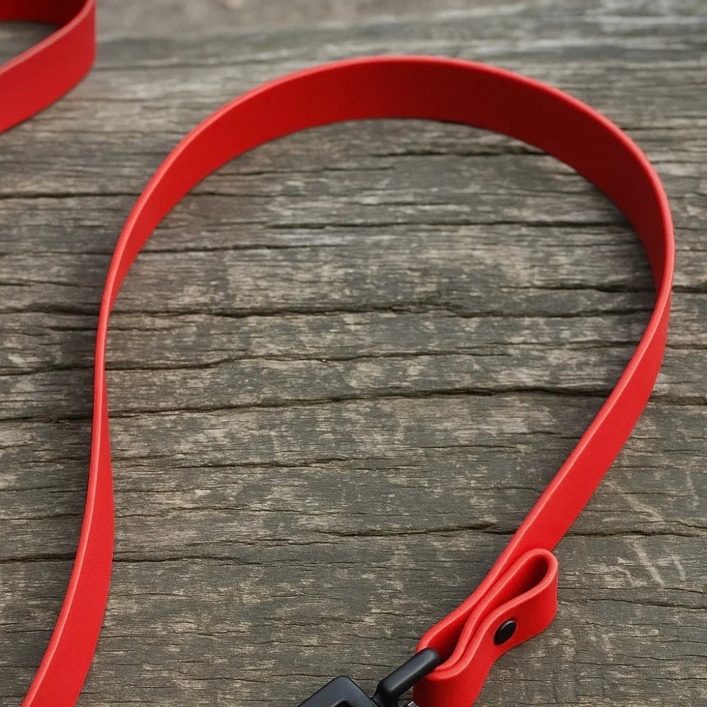 Red Biothane dog lead with black hardware on rustic wooden surface