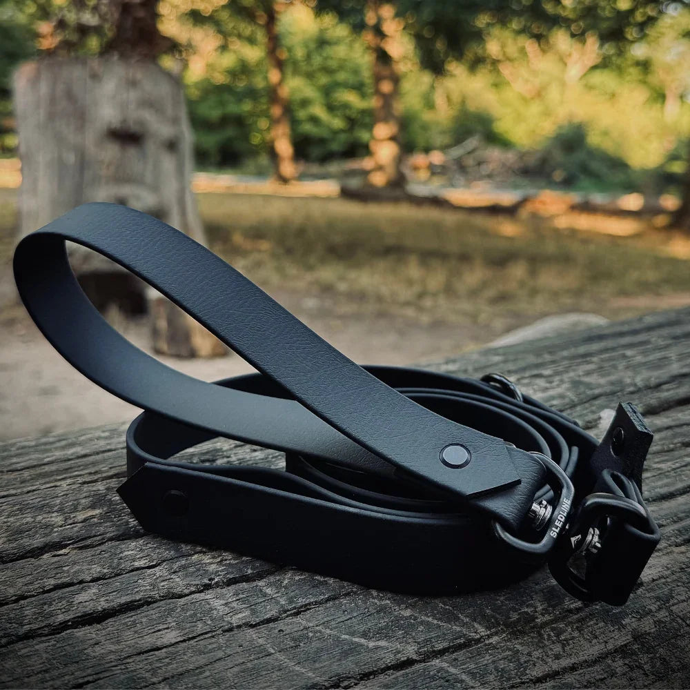 Black Biothane dog lead with metal hardware on wood outdoors