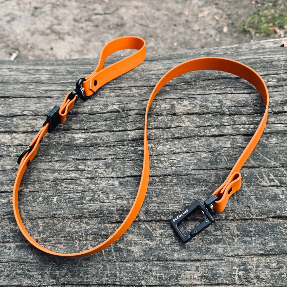 Orange Biothane dog lead with metal hardware on rustic wooden surface