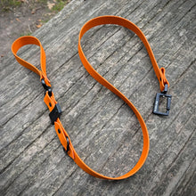 Orange Biothane dog lead with black hardware on wooden surface