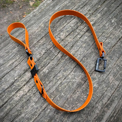 Orange Biothane dog lead with black hardware on wooden surface