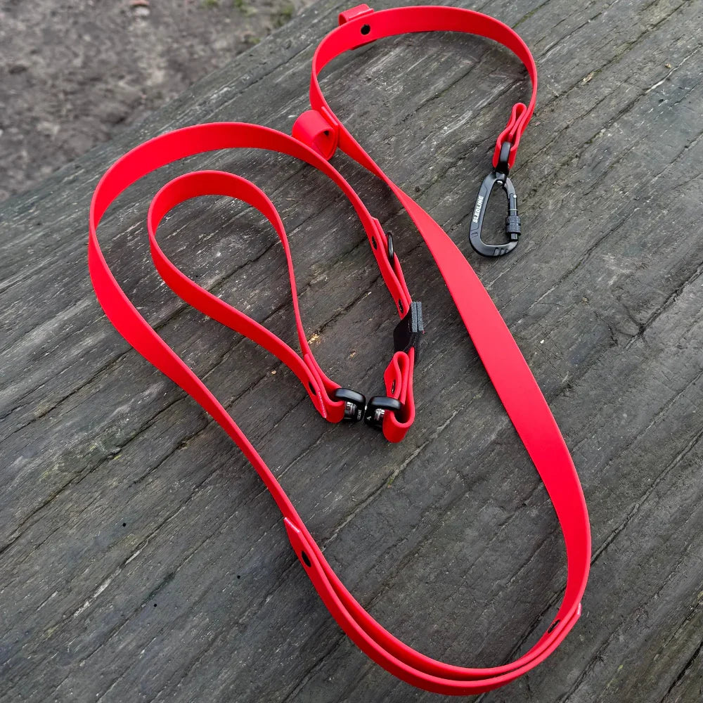 Red Biothane dog lead with black strength-tested hardware on wooden surface