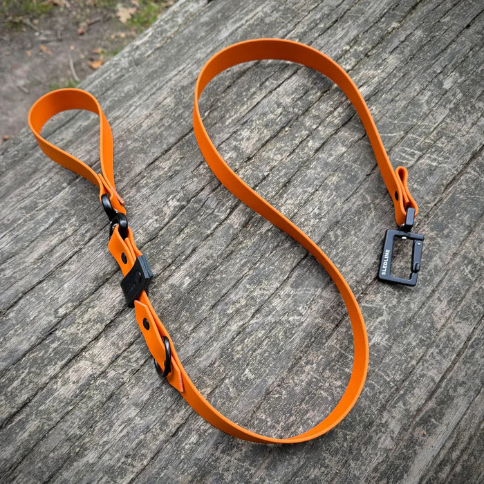 Orange Biothane dog lead with black hardware on wooden surface